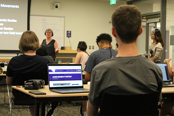 Dr. Heather Evans at the University of Washington teaches a group of students with disabilities. A student laptop can be seen in the forefront with a webpage about Learning Disability History.
