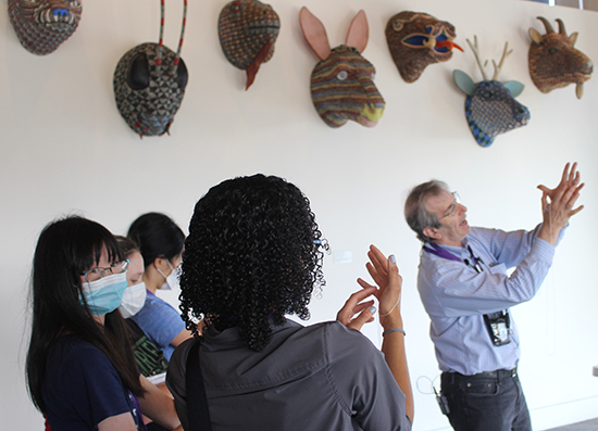 Eric Chudler makes shapes with his hands for.a fews students in front of a wall of animal masks.