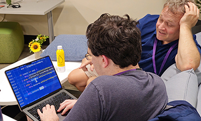An instructor points towards an inlarged laptop screen while a student types.
