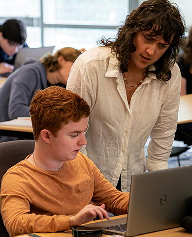 An instructor works with a student on a laptop.
