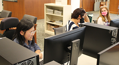 Three students working at computers in a library.