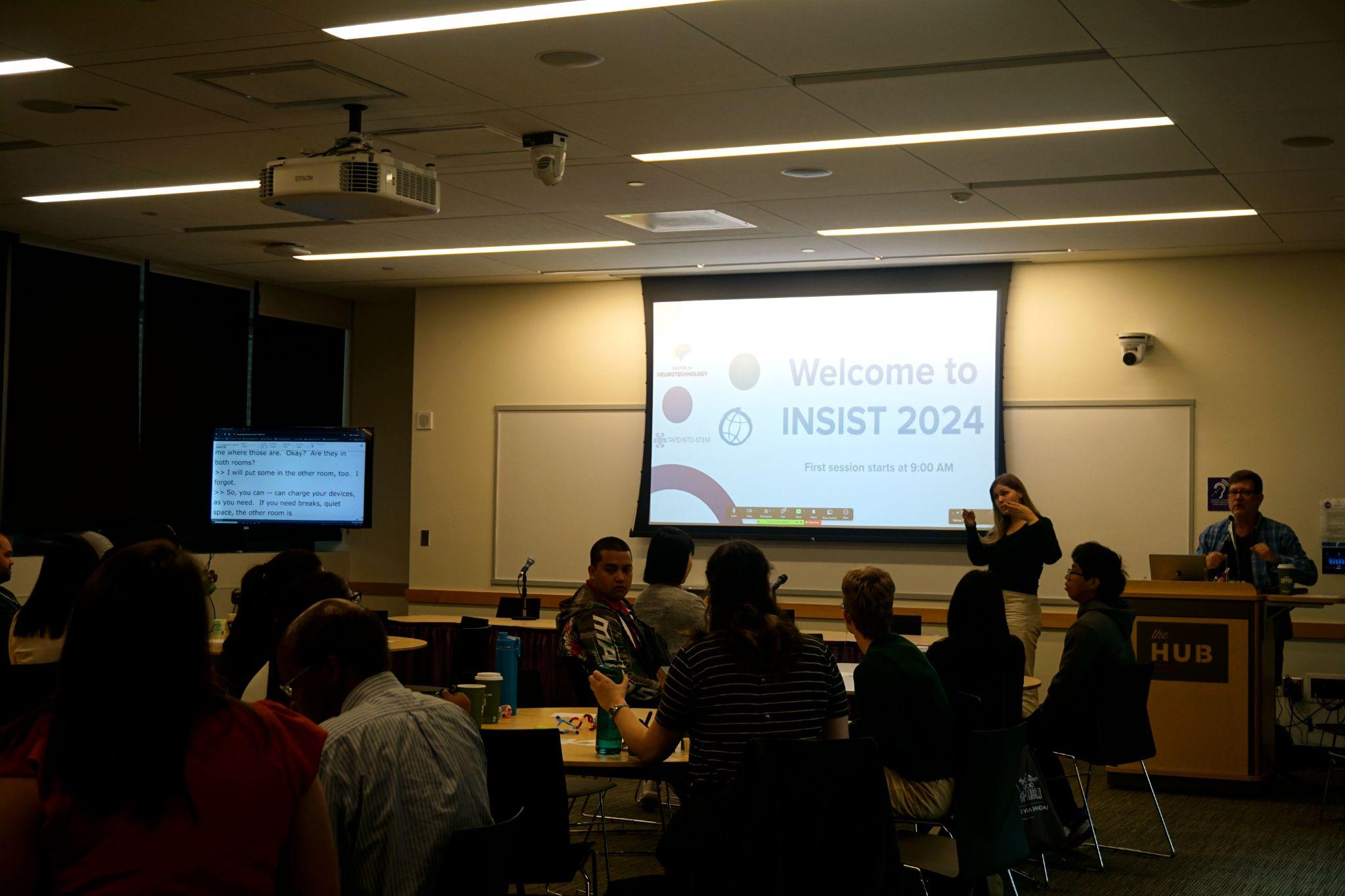 Attendees in a classroom with a speaker, interpreter, and powerpoint.
