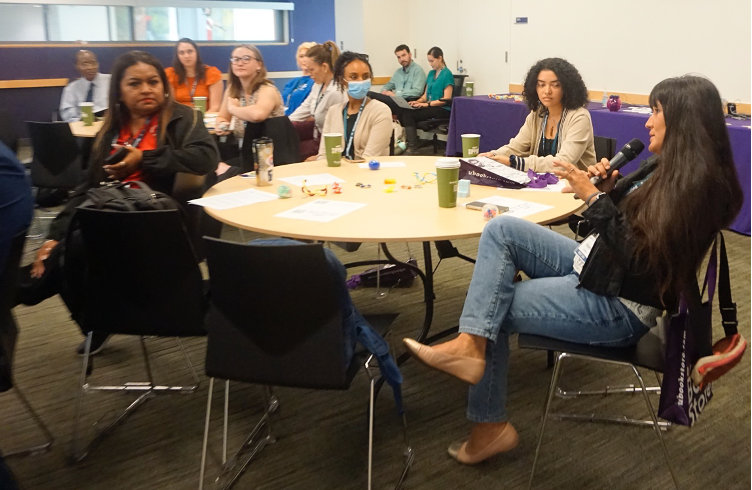 One participant speaks into a microphone while others look and listen.
