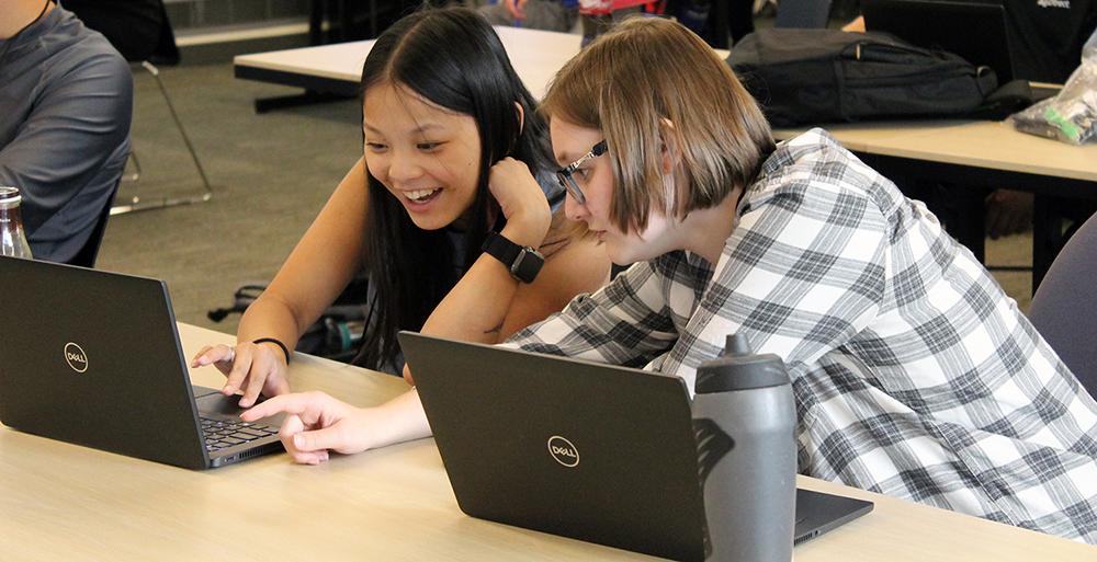 Two students look at laptops together.
