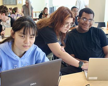 Two Scholars collaborate at laptops in a classroom, with a DO-IT staff member assisting them.