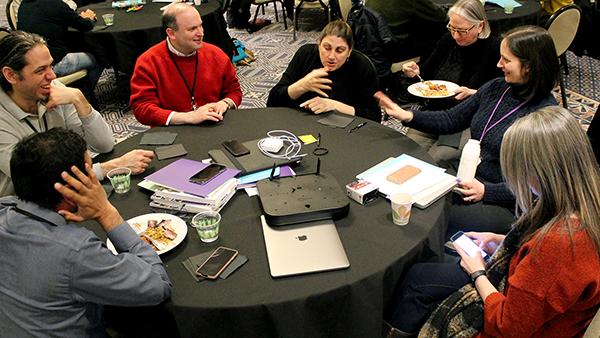 Attendees from the AccessINCLUDES Conference talking around a table.
