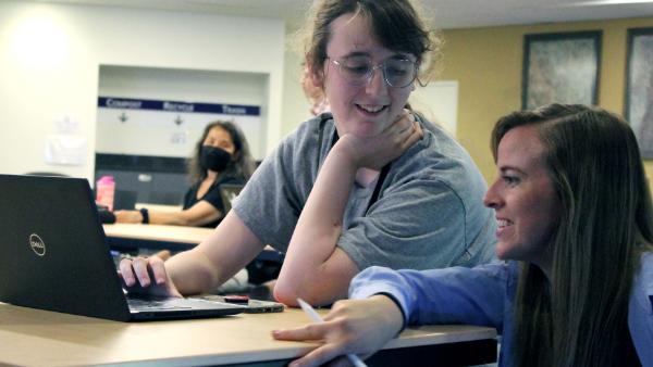 A instructor and a student working together at a laptop in a classroom.