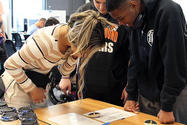 Three students look at a project on a table.