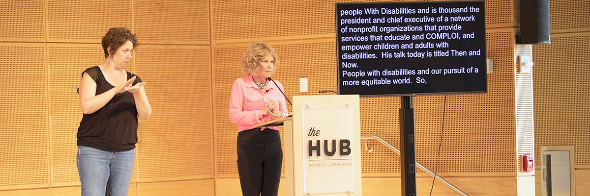 DO-IT Founder Sheryl Burgstahler speaks to a room of people while using both a sign language interpreter and live captions.