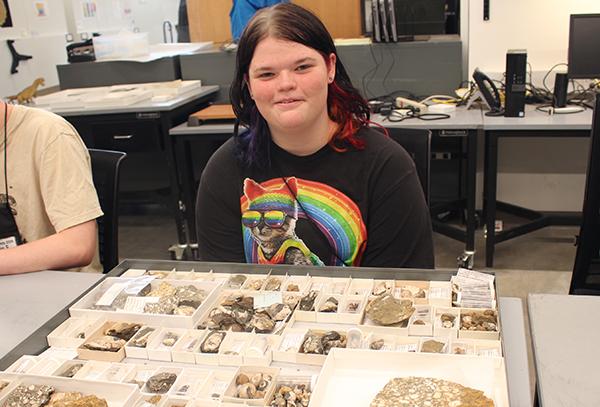 A student in a cat shirt sits at a table with a variety of fossils.