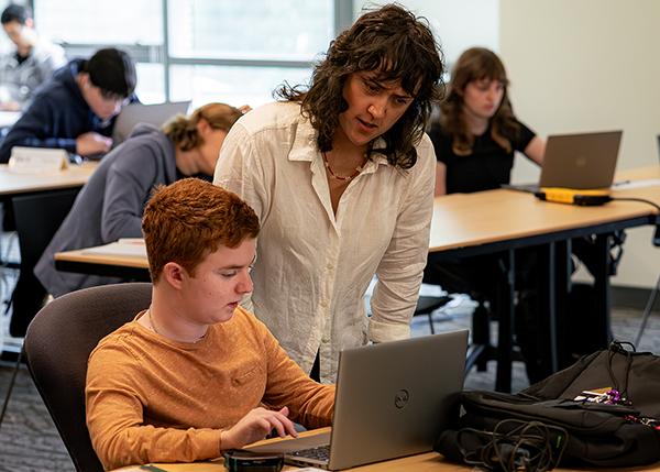 An instructor works with a student on a laptop.