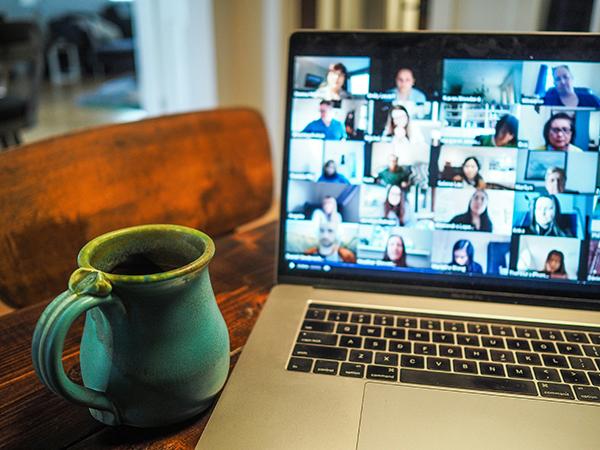 A mug sits next to a laptop screen showing a number of people in a Zoom call