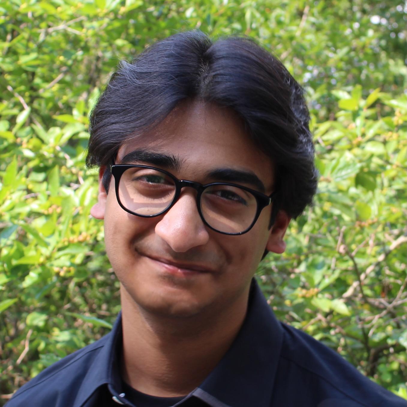Headshot of Ritesh with green foliage in the background.