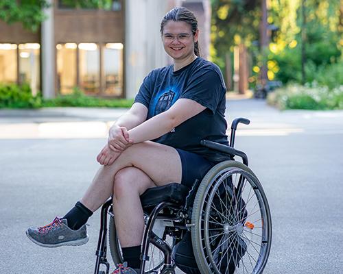 Piper sits on a wheelchair and smiles.
